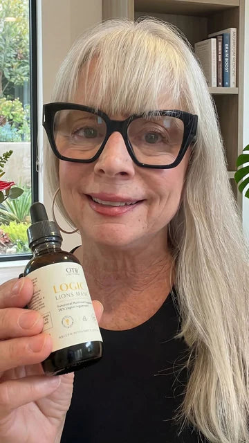 Senior woman holding a bottle of Logic Lion's Mane supplement indoors.