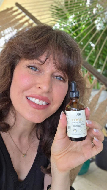 Woman holding a bottle of Logic Lion's Mane supplement indoors.