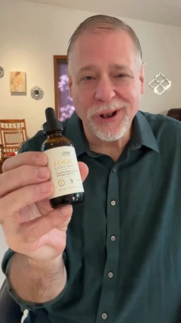 Senior man holding a bottle of Logic Lion's Mane with a blurred indoor background
